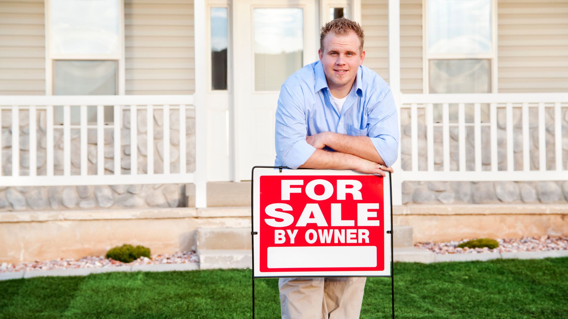 A man holding down a "For Sale" sign in front of his house